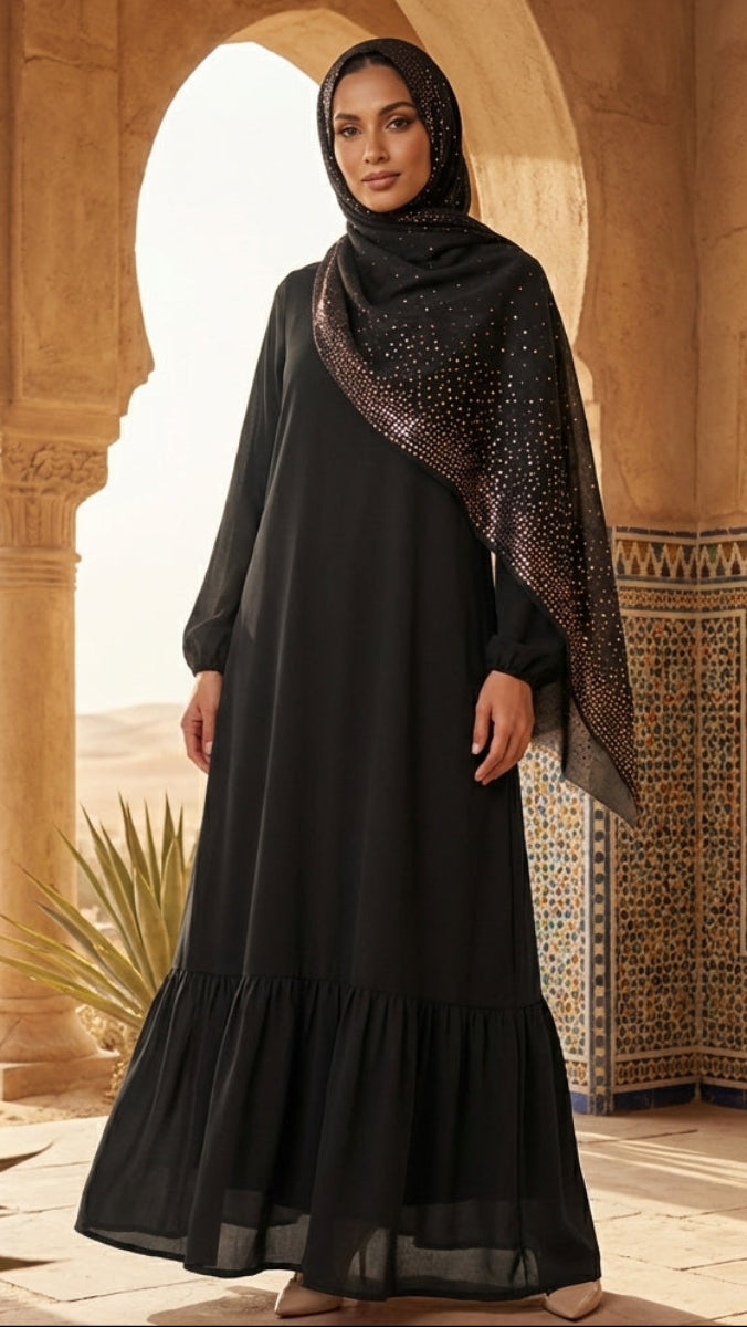 Woman in a black dress and hijab standing in a sunlit architectural setting with plants.