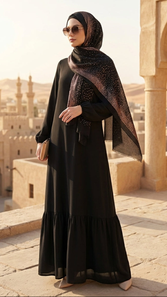 Woman in a black abaya with a patterned shawl standing in front of an architectural structure with arches.