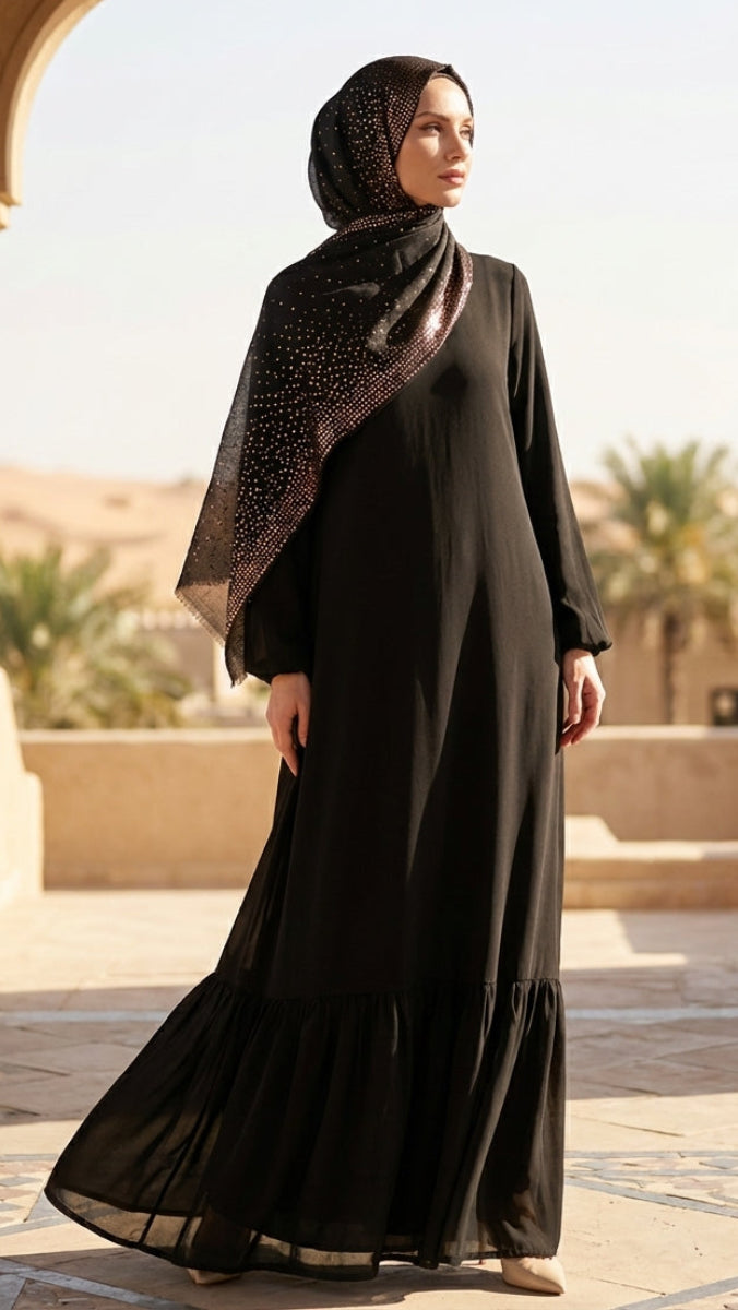 Woman in a black abaya with a patterned scarf standing in front of an archway.