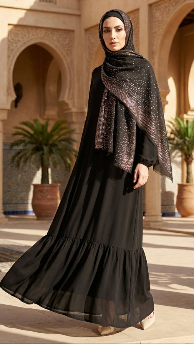 Woman in a black abaya with a patterned shawl standing in an architectural courtyard.