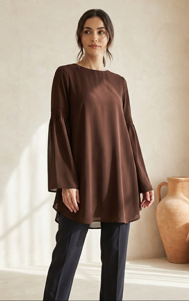 Woman wearing a brown dress standing in a room with decorative vases.