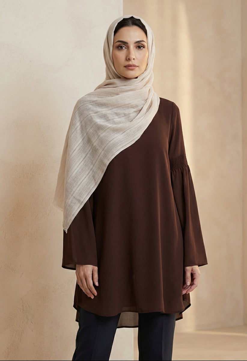 Woman wearing a brown top and beige hijab against a neutral background