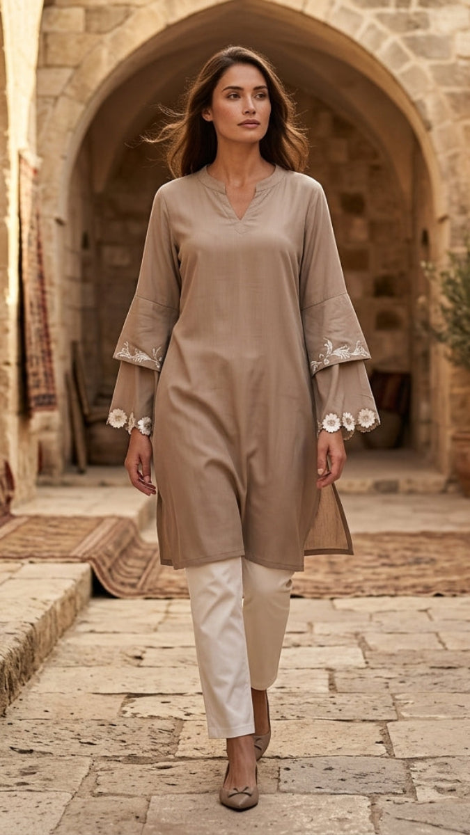 Woman in a beige outfit walking through an arched stone passageway.
