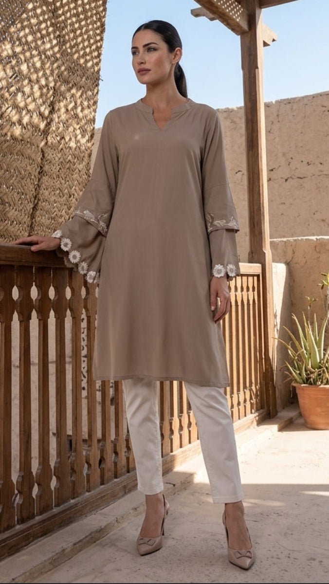 Woman in a beige outfit standing on a rooftop with a textured wall and plants in the background