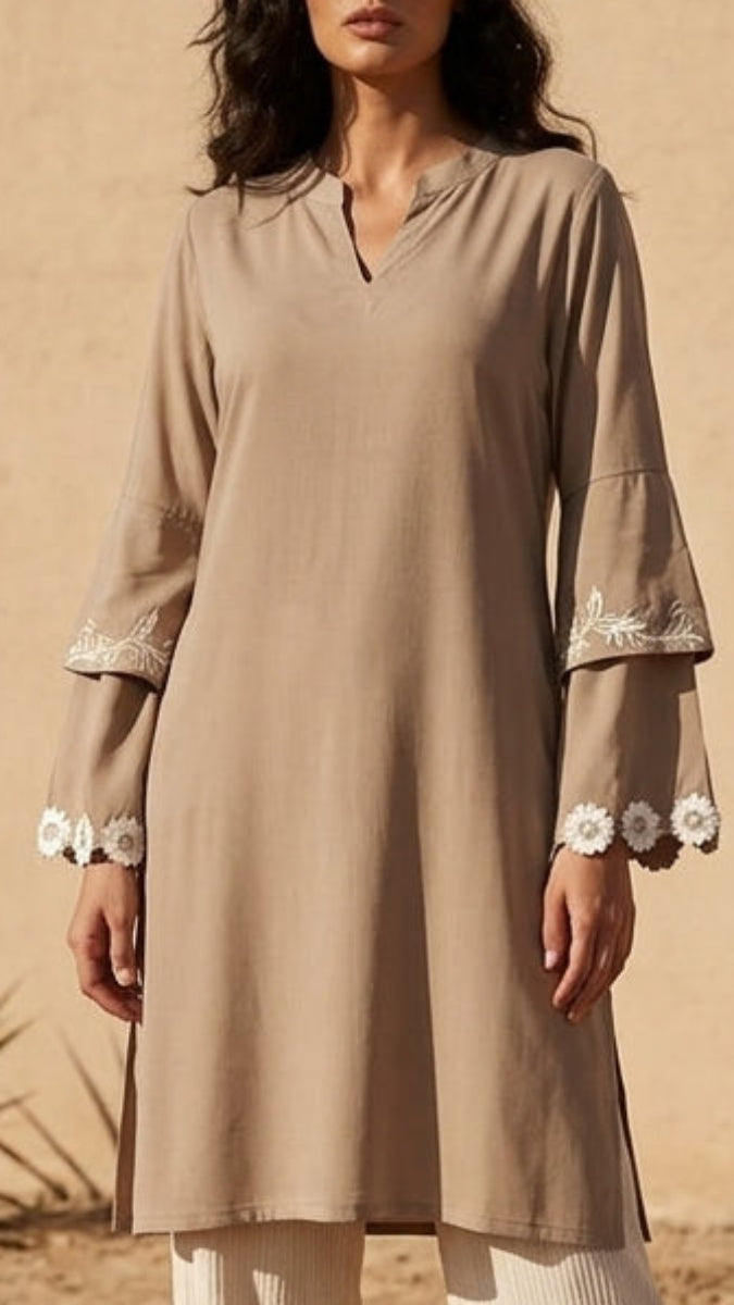 Woman in a beige outfit standing in a desert landscape with a beige wall.