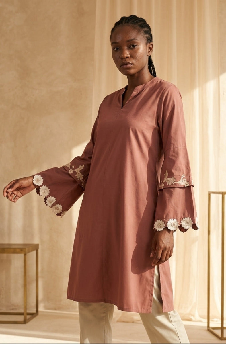 Woman wearing a pink dress with floral embroidery in a softly lit room.