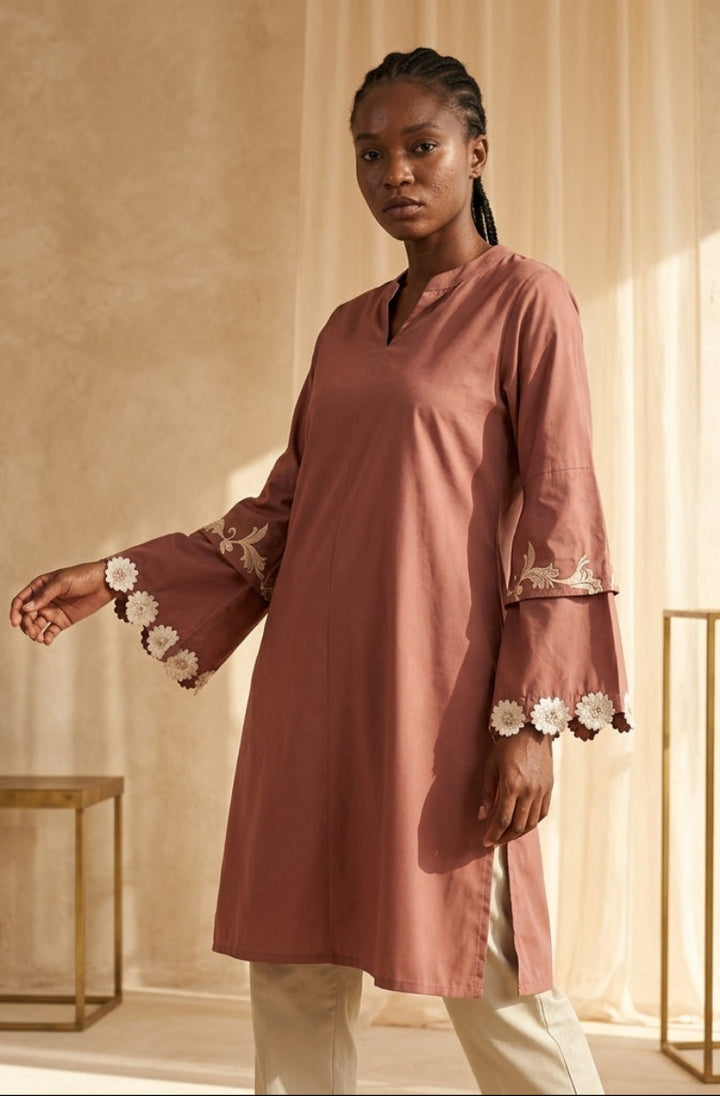 Woman wearing a pink dress with floral embroidery in a softly lit room.