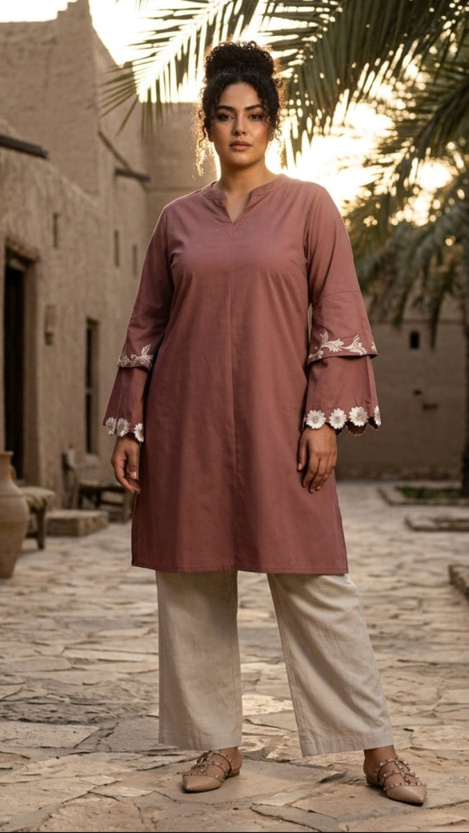 Woman in a pink traditional outfit standing in a sunlit alleyway with palm trees.