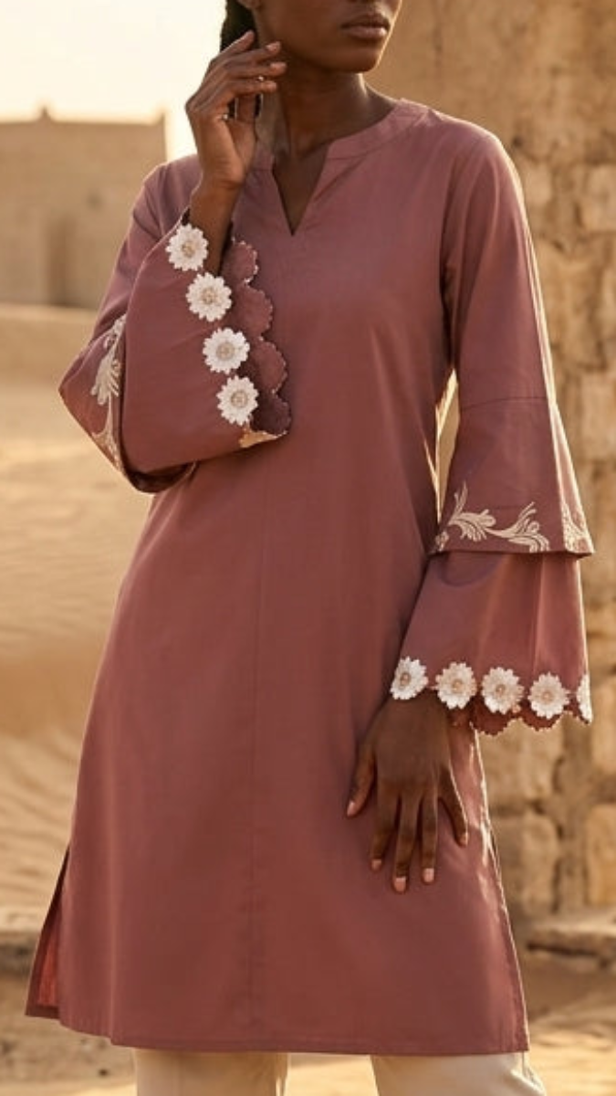 Woman wearing a mauve dress with white floral embroidery against a stone wall background