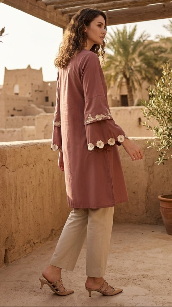 Woman in a pink dress standing on a balcony with a desert village view.