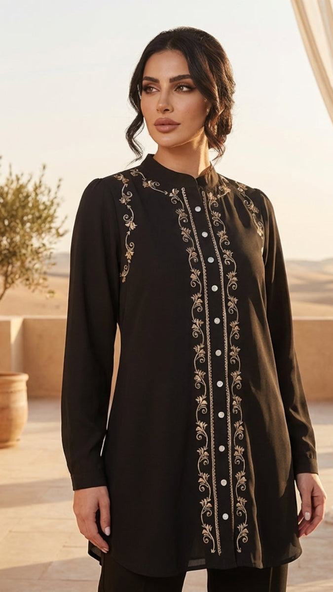 Woman wearing a black embroidered dress in an outdoor setting with plants and curtains.