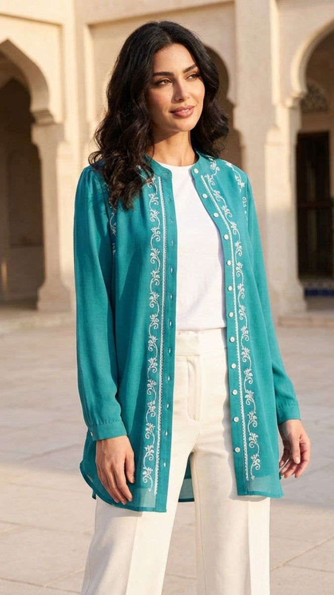 Woman wearing a teal embroidered jacket in an outdoor setting with arches and tiles.