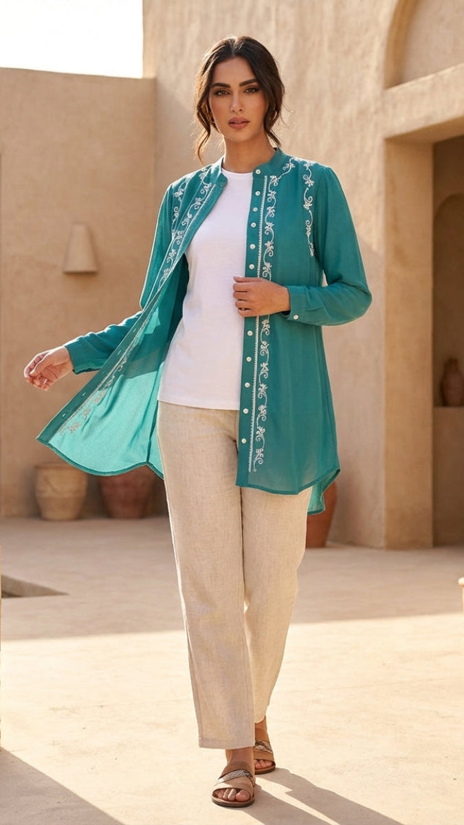 Woman wearing a teal embroidered top and beige pants in an outdoor setting.