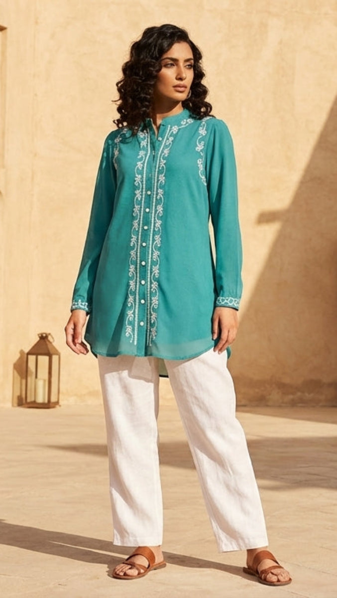 Woman in teal top and white pants standing in a sunlit courtyard with arches and potted plants.
