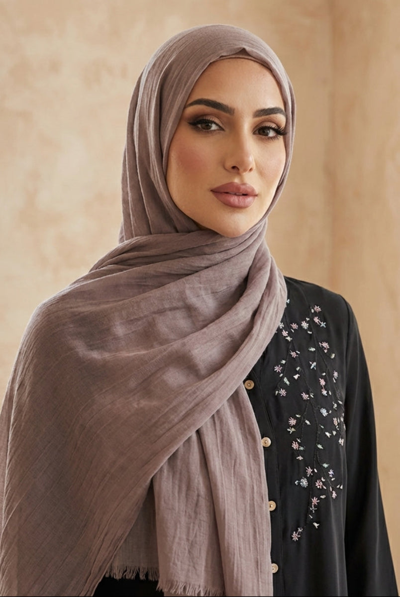 Woman wearing a beige hijab and black outfit with floral patterns indoors.