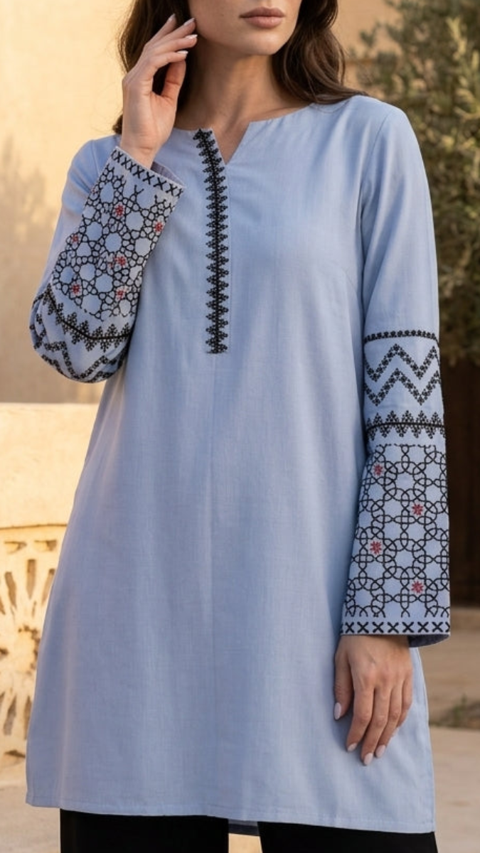 Woman wearing a light blue embroidered dress standing in front of a decorative wall.