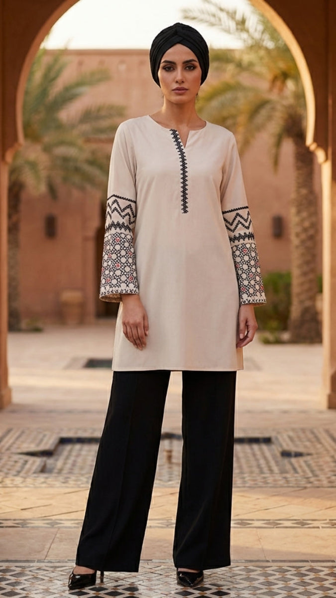 Woman wearing a beige top with black and white patterns and black pants in an outdoor setting.