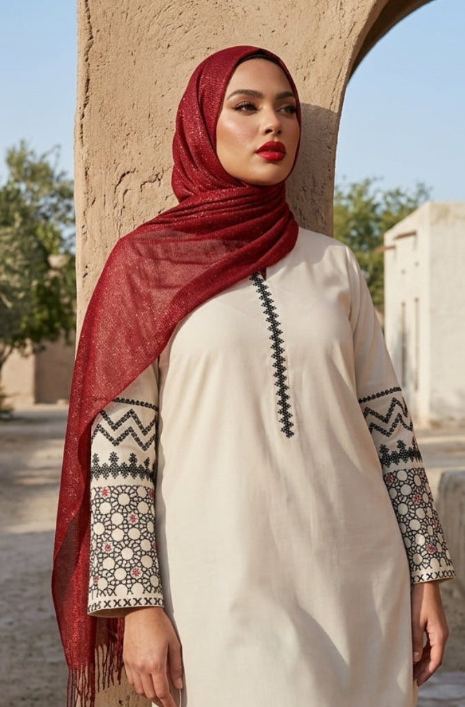 Woman wearing a red hijab and patterned white top standing in front of a stone building.