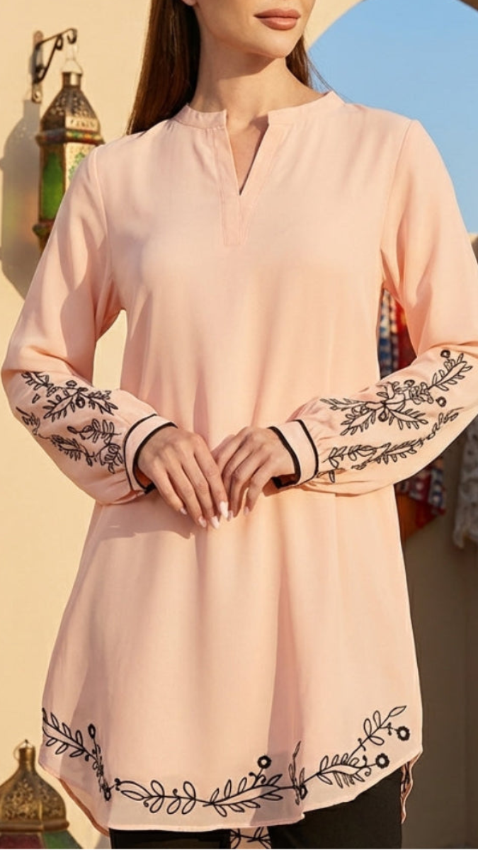 Light pink long-sleeve top with black floral embroidery on a blurred background