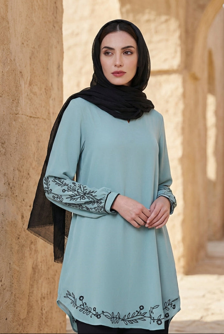 Woman wearing a light blue dress with black embroidery in an arched stone corridor.