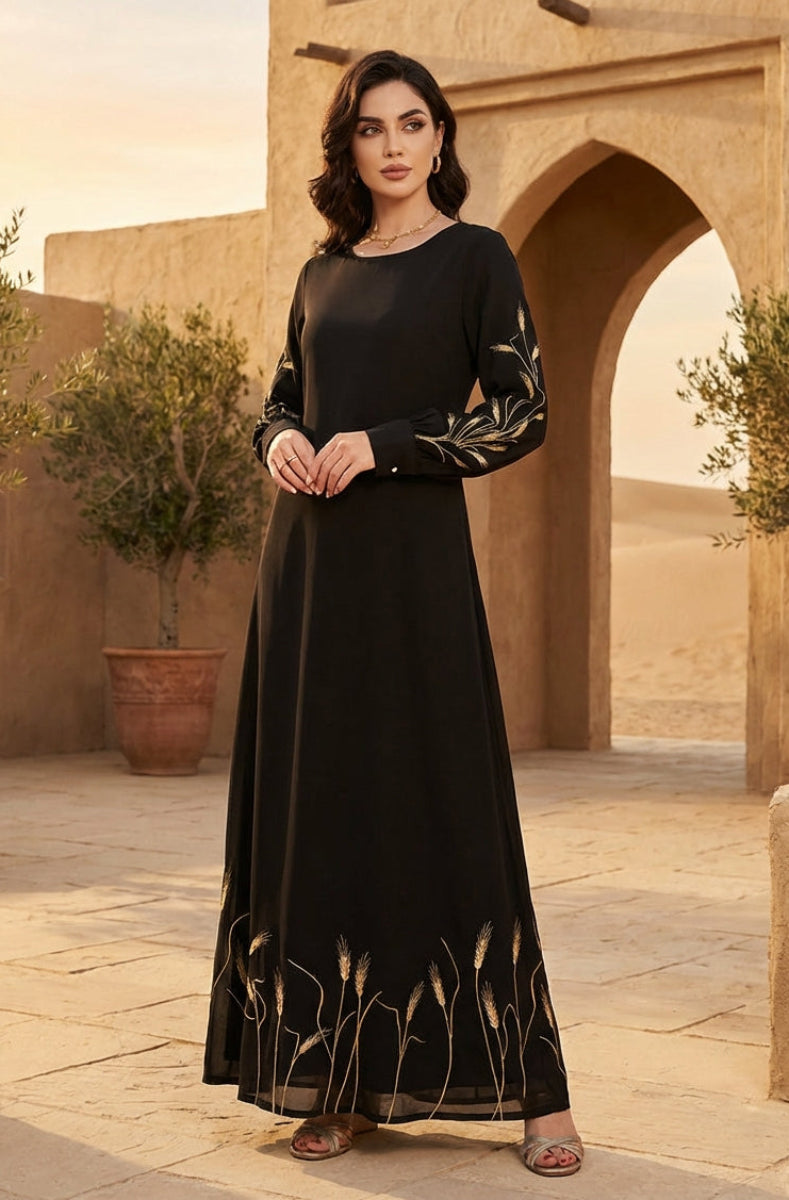 Woman in a black dress with gold embroidery standing in a desert setting with arches and potted plants.