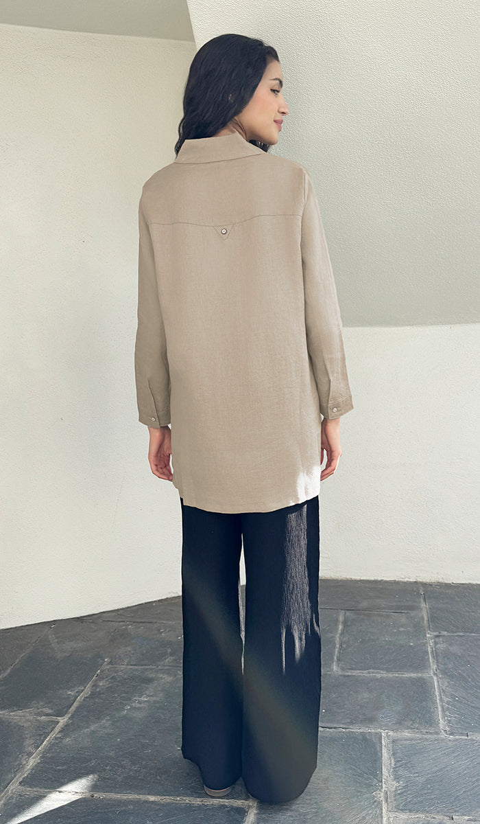 Woman wearing a beige long-sleeve shirt and dark pants in a minimalistic setting
