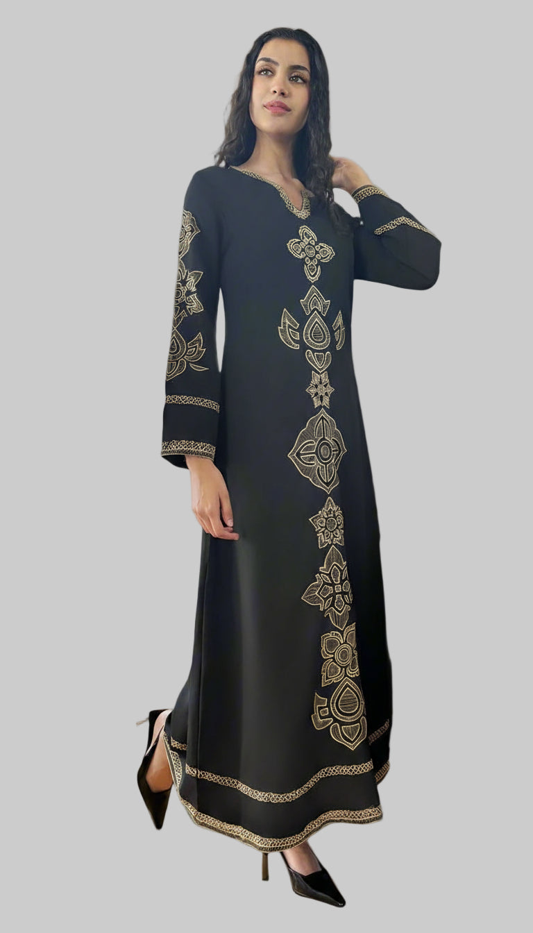 Woman in a black dress with gold embroidery standing in a room with a piano and open door.