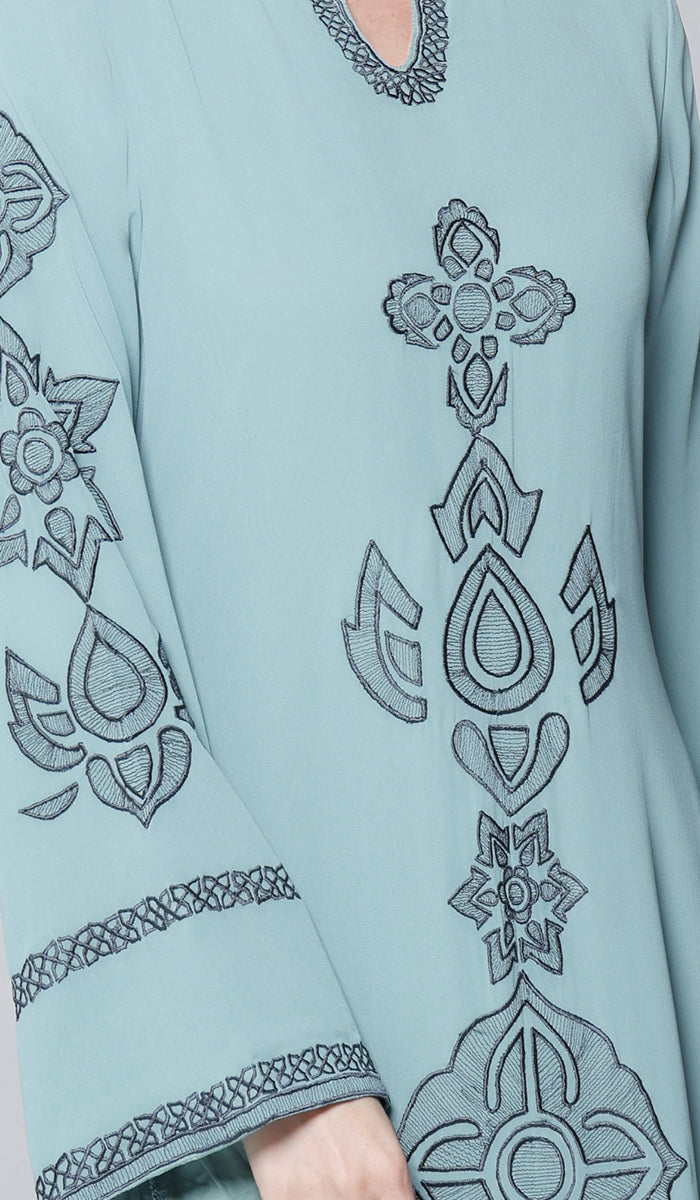 Light blue garment with intricate black embroidery on sleeves and chest.