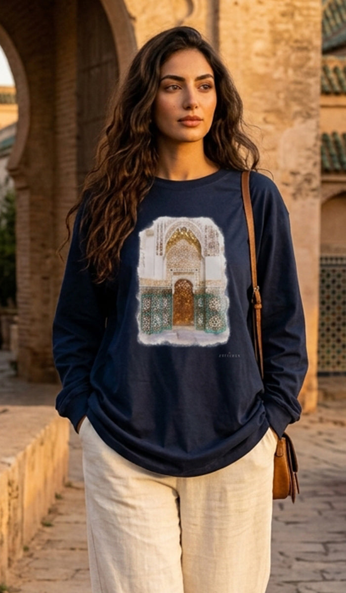 A woman wearing a navy blue long-sleeve t-shirt with a large graphic print of an archway, paired with cream linen pants, standing in front of a warm stone archway.