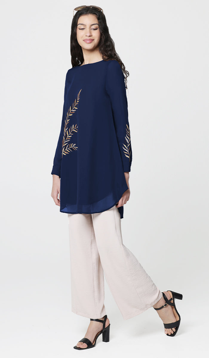 Woman wearing Baraka tunic in Sapphire with white pants and black heels. 