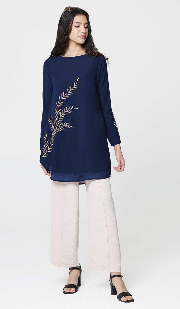Woman wearing modest Baraka tunic in Sapphire with white pants and heels. 