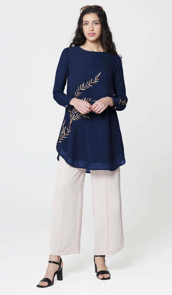 Woman wearing sunglasses with Baraka tunic in Sapphire with white pants and heels. 