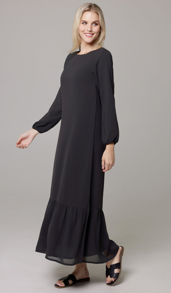 Woman smiling wearing Batool dress in Black with sandals. 