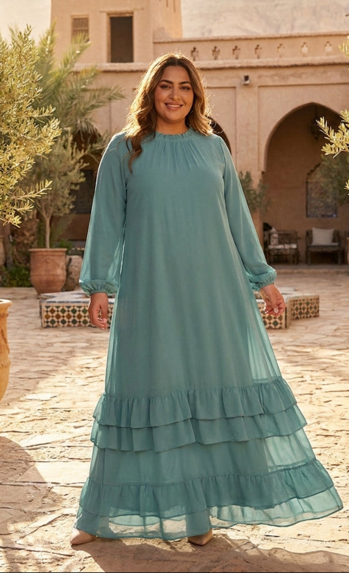 Woman in a teal dress standing in an outdoor setting with architectural elements and plants.