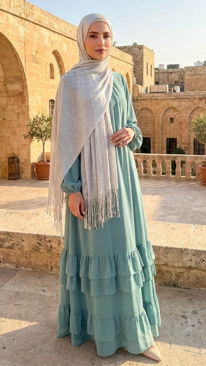 Woman in a light blue dress and hijab standing in front of historical architecture.