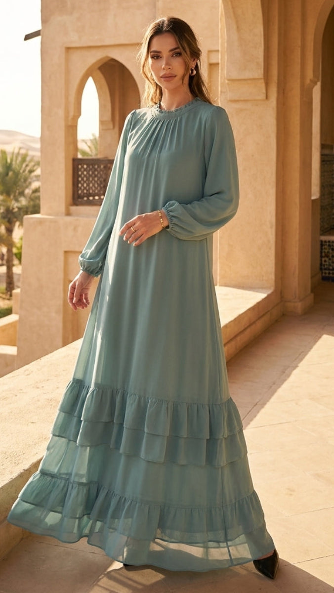 Woman in a teal dress standing on a sunlit patio with architectural elements and palm trees in the background.