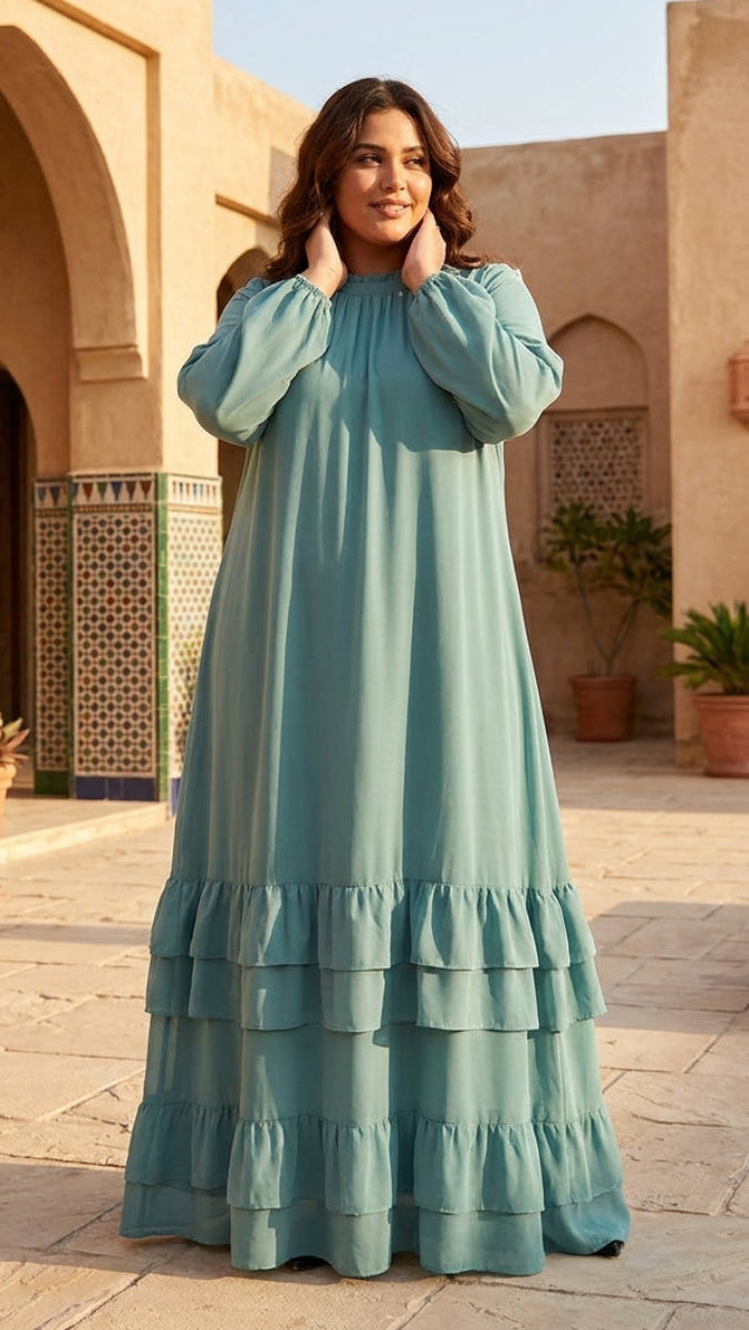 Woman in a teal dress standing in an outdoor courtyard with arches and plants.