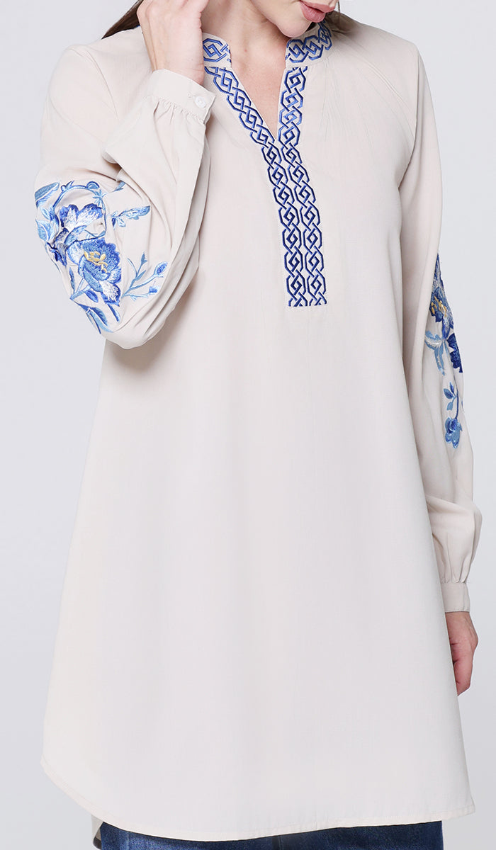 Beige long-sleeve top with blue floral and geometric embroidery on a white background