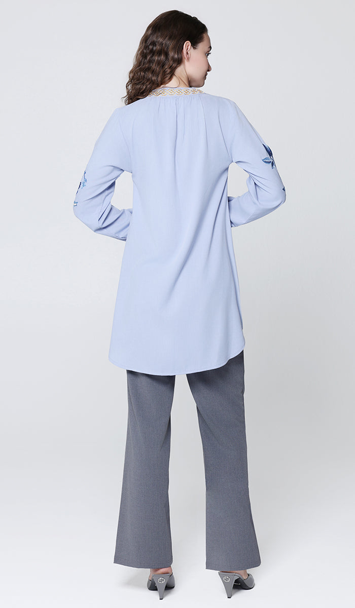 Woman wearing a light blue top and gray pants on a white background