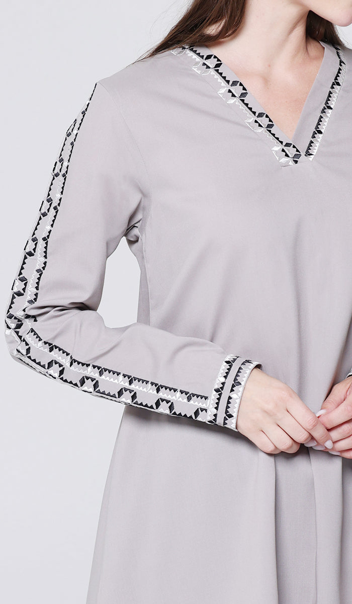 Gray dress with black and white patterned trim on sleeves and neckline against a light gray background