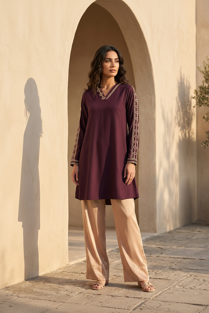 Woman wearing a maroon dress with gold embroidery in front of a beige wall.