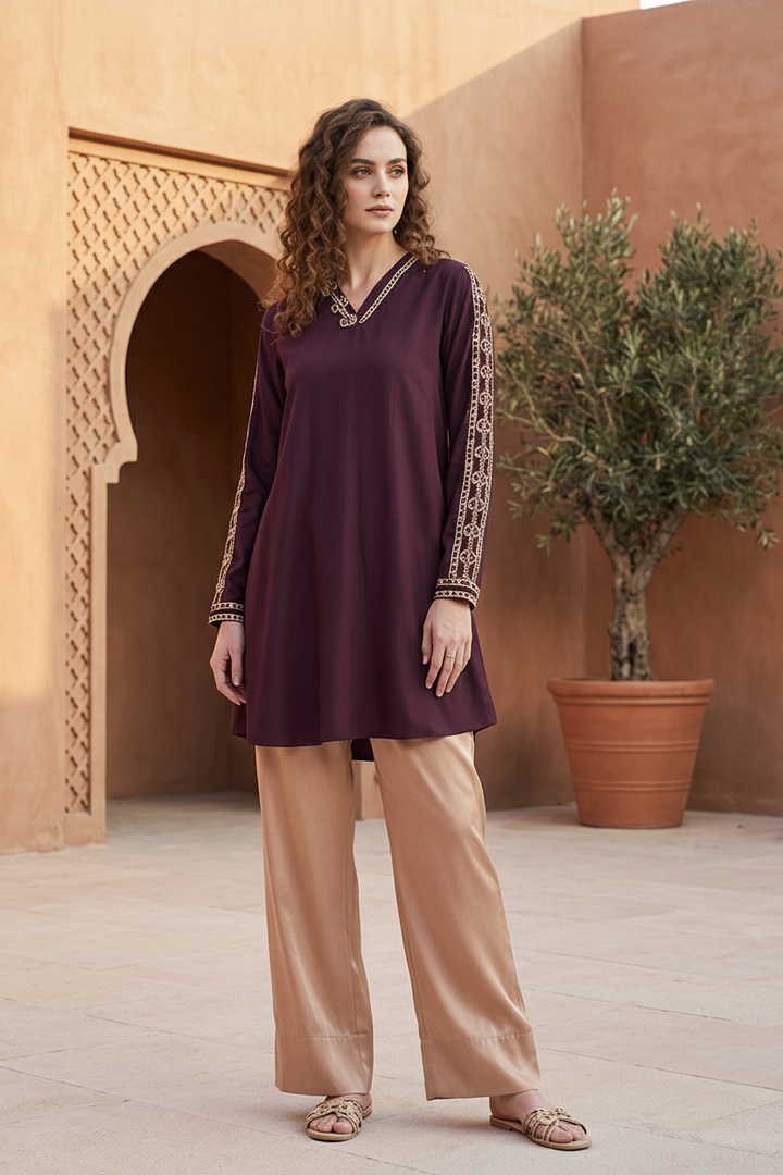Woman wearing a dark purple top with gold accents and beige pants in an outdoor setting.