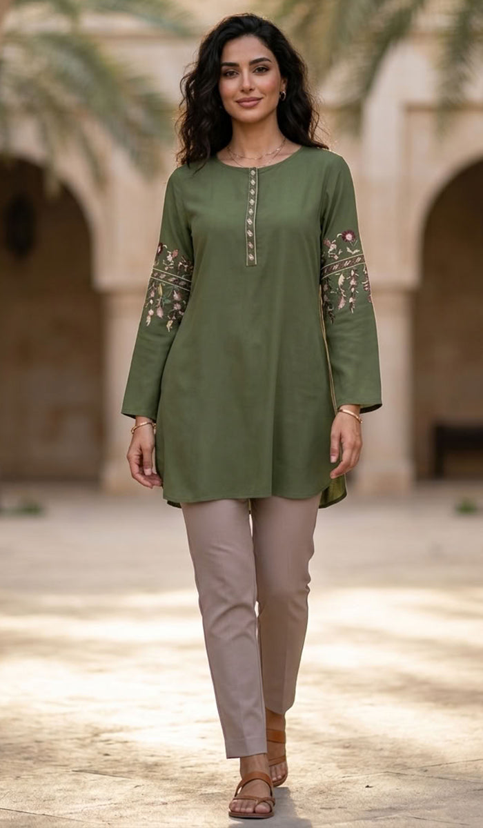 A woman modeling a sage green long-sleeve kurta with floral embroidery on the sleeves and a buttoned neckline, paired with beige trousers, in an outdoor courtyard setting.