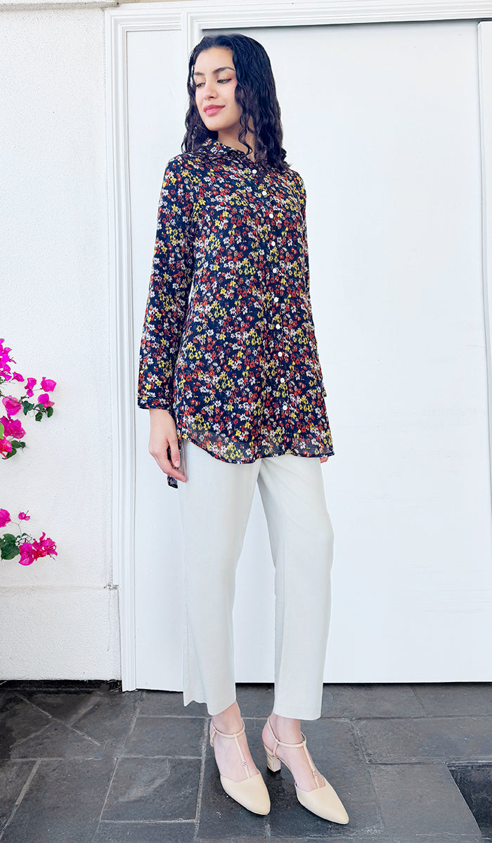 Woman wearing a floral dress and white pants standing in front of a white door.