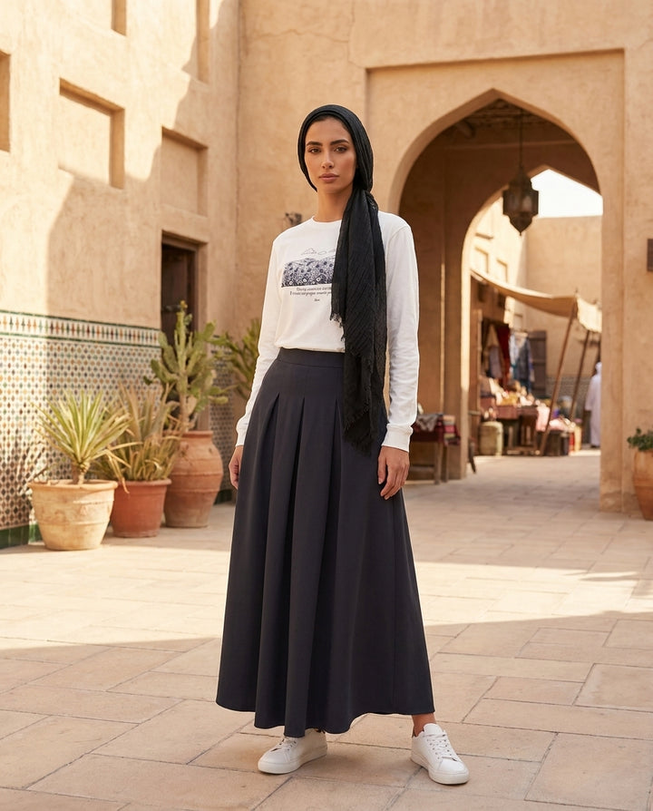 Woman in a white long-sleeve shirt and black skirt standing in an outdoor setting with architectural elements.
