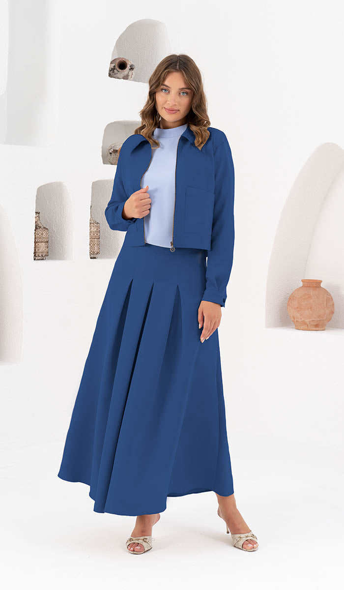 Woman standing in front of bookshelf wearing Mia skirt in Indigo with Mia jacket in Indigo. 