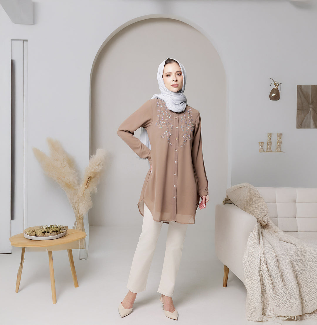 Woman in a beige top and white pants standing in a modern living room.