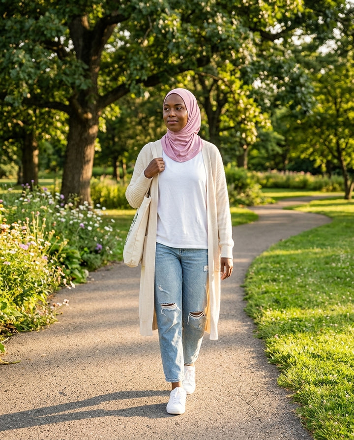 Woman walking on a path in a park wearing a hijab, long cardigan, and jeans.