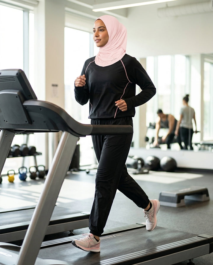 Woman wearing a pink hijab and black athletic wear on a treadmill in a gym.