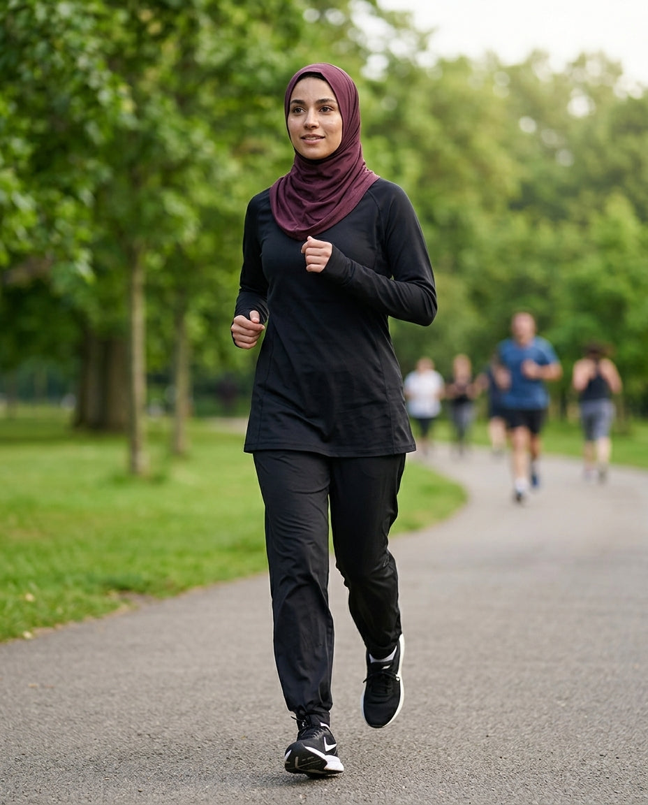 Woman running in a park wearing a black outfit and maroon hijab.